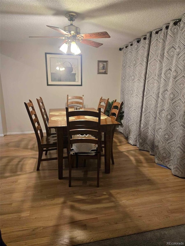 dining room with baseboards, a textured ceiling, ceiling fan, and wood finished floors