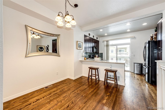 kitchen with dark wood-type flooring, an inviting chandelier, a kitchen breakfast bar, black fridge, and kitchen peninsula