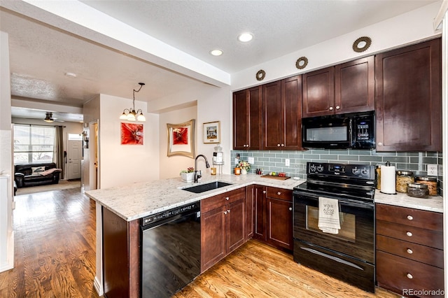 kitchen with black appliances, a sink, light wood finished floors, a peninsula, and a textured ceiling