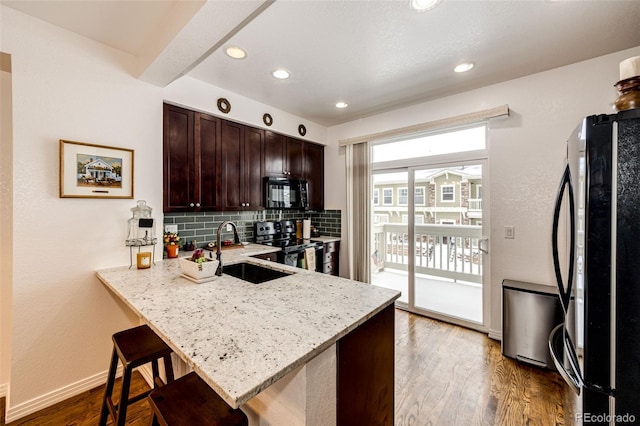 kitchen featuring black appliances, a sink, tasteful backsplash, a breakfast bar, and light stone countertops
