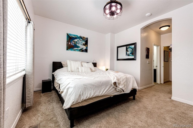 carpeted bedroom featuring arched walkways and baseboards