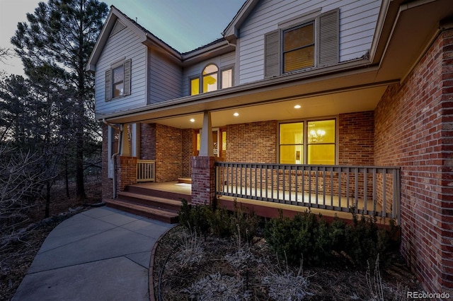 view of exterior entry with brick siding and a porch