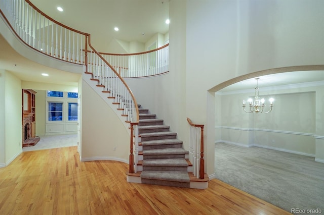 stairway featuring arched walkways, a notable chandelier, wood finished floors, and a towering ceiling