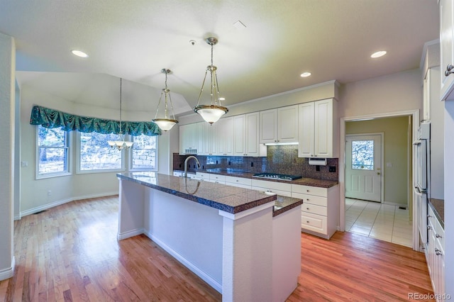 kitchen with a center island with sink, light wood-style flooring, tasteful backsplash, white cabinets, and a healthy amount of sunlight