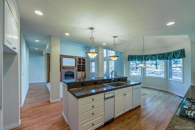 kitchen featuring light wood-style floors, white dishwasher, a glass covered fireplace, white cabinetry, and a sink