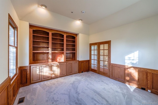 unfurnished office with visible vents, a wainscoted wall, lofted ceiling, french doors, and light carpet