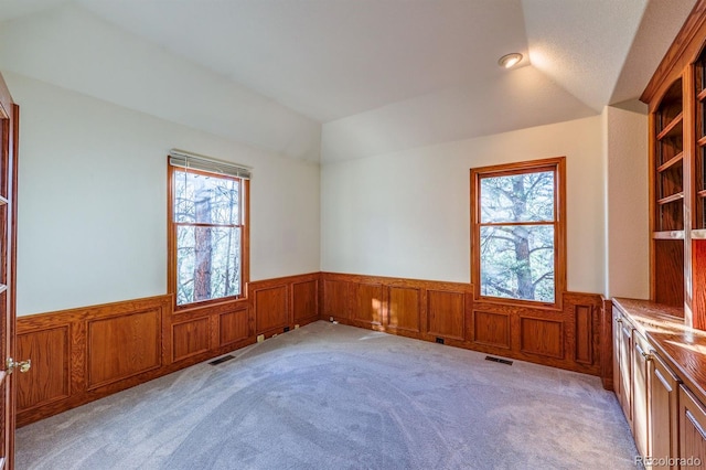 empty room with a wainscoted wall, lofted ceiling, light colored carpet, and visible vents