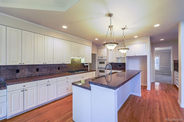 kitchen featuring light wood finished floors, white double oven, decorative backsplash, white cabinetry, and a sink