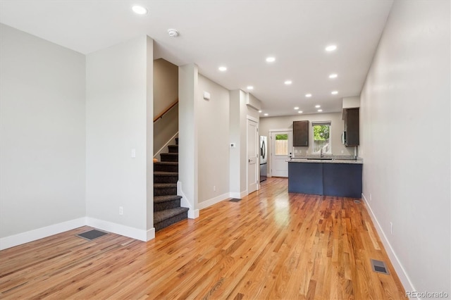 unfurnished living room featuring light wood-type flooring, stairs, recessed lighting, baseboards, and a sink