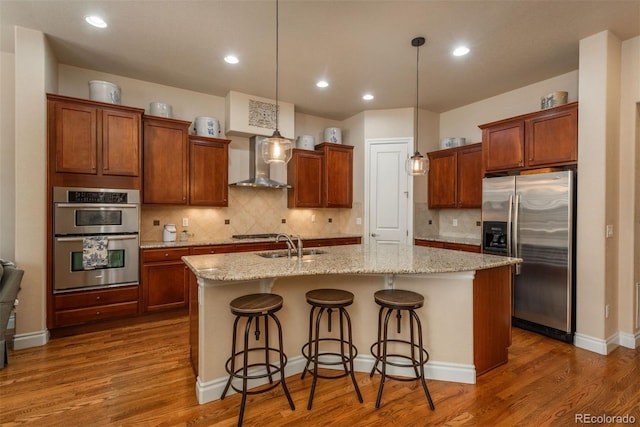 9165 Kornbrust Dr, Lone Tree, CO 80124 - kitchen featuring stainless steel appliances, wall chimney exhaust hood, a sink, a center island with sink, and wood finished floors