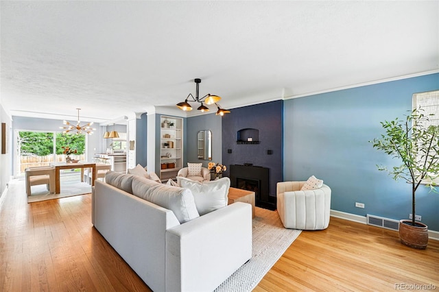living area featuring a chandelier, baseboards, a large fireplace, and wood finished floors