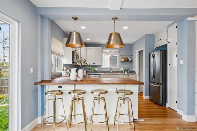 kitchen featuring stainless steel appliances, butcher block counters, a sink, a peninsula, and recessed lighting
