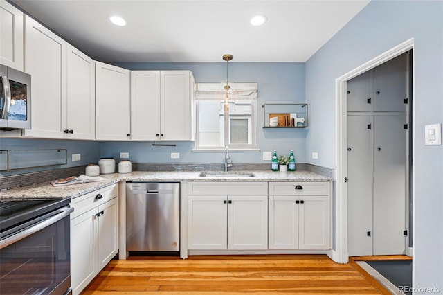 kitchen featuring a sink, stainless steel appliances, light wood-style floors, white cabinetry, and hanging light fixtures