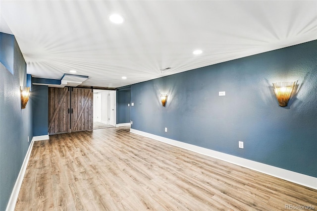 empty room with a barn door, recessed lighting, light wood finished floors, and baseboards