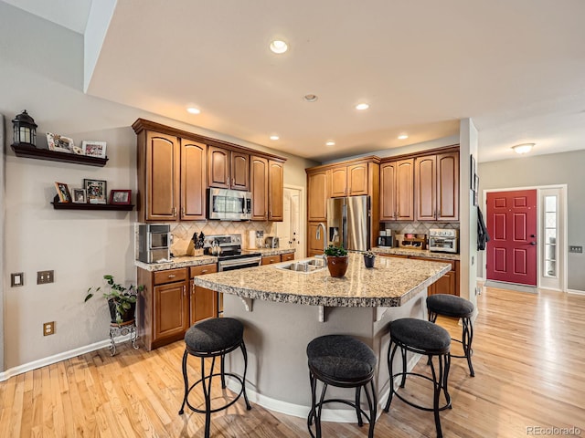 kitchen featuring sink, a breakfast bar area, appliances with stainless steel finishes, an island with sink, and light hardwood / wood-style floors