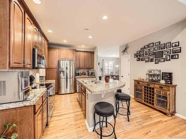 kitchen featuring appliances with stainless steel finishes, an island with sink, sink, a kitchen breakfast bar, and light stone counters