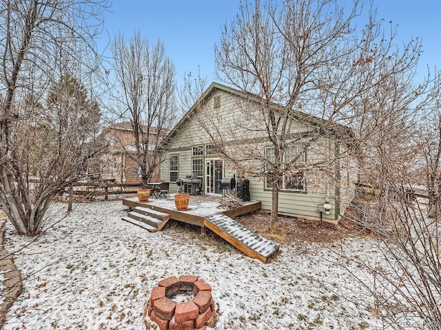 snow covered rear of property featuring a wooden deck and a fire pit