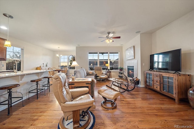 living room with ceiling fan with notable chandelier, light wood-type flooring, a healthy amount of sunlight, and a tiled fireplace