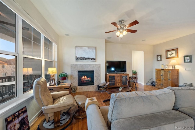 living room with ceiling fan, wood-type flooring, and a tiled fireplace