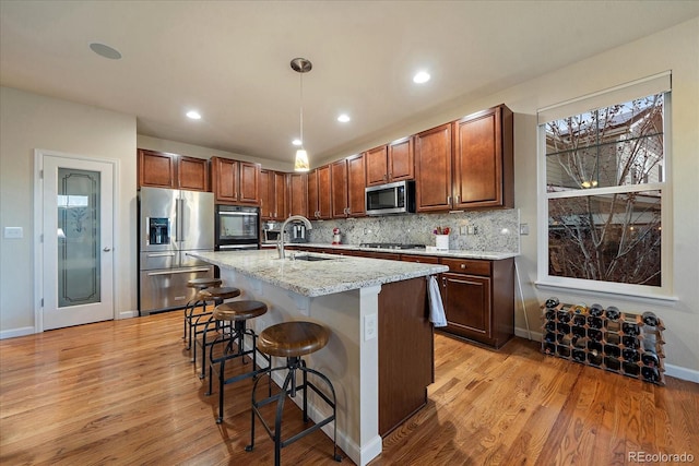 kitchen with light stone countertops, appliances with stainless steel finishes, sink, light hardwood / wood-style flooring, and an island with sink