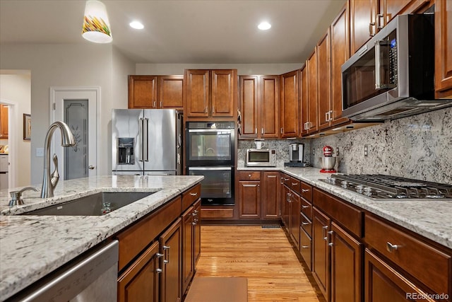 kitchen featuring light stone countertops, sink, decorative backsplash, appliances with stainless steel finishes, and light wood-type flooring