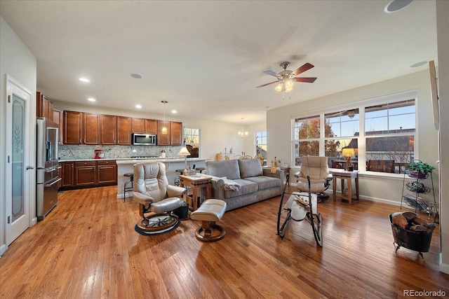 living room with ceiling fan with notable chandelier and light hardwood / wood-style floors