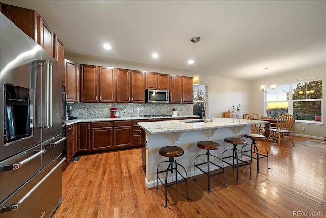 kitchen with hanging light fixtures, a kitchen breakfast bar, light hardwood / wood-style floors, a center island with sink, and appliances with stainless steel finishes