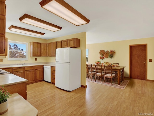 kitchen with light wood finished floors, white appliances, light countertops, and a sink