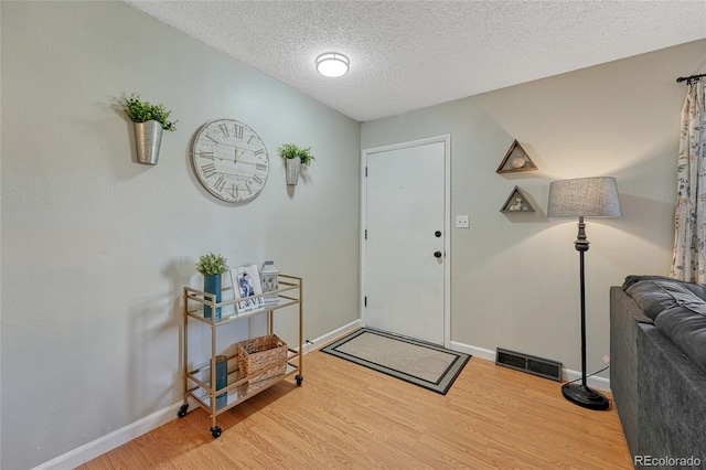 entryway with baseboards, visible vents, wood finished floors, and a textured ceiling