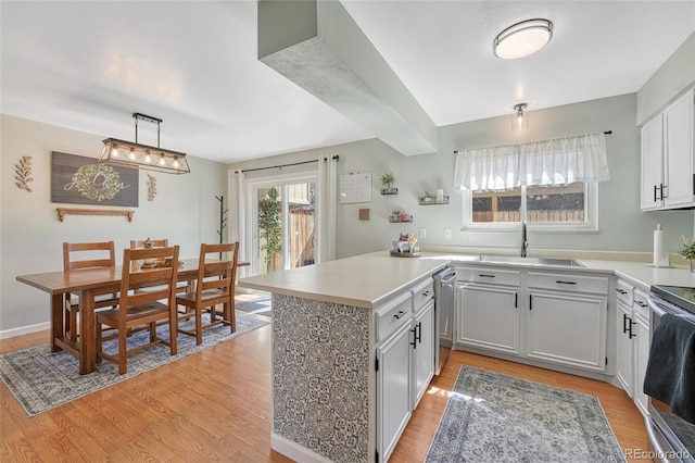 kitchen featuring light wood finished floors, a peninsula, a sink, and stainless steel appliances