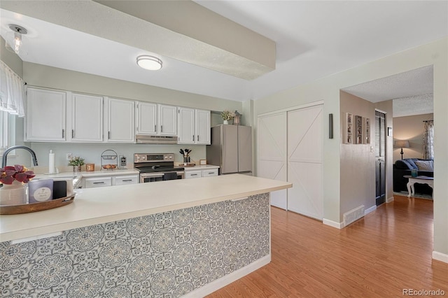 kitchen featuring light countertops, freestanding refrigerator, a peninsula, under cabinet range hood, and electric stove