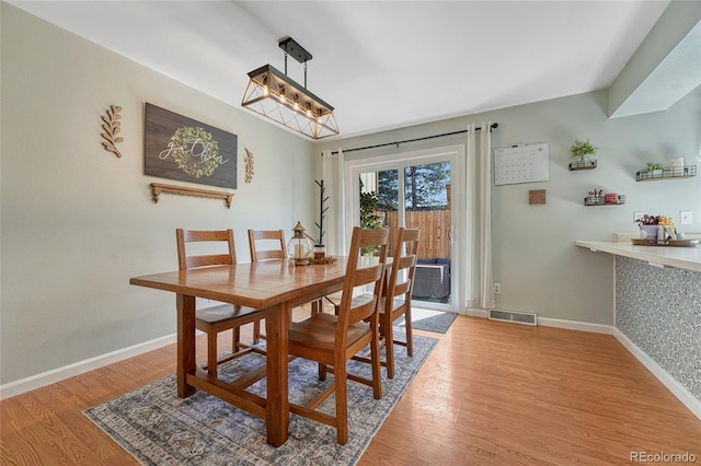 dining space with light wood-type flooring, a notable chandelier, baseboards, and visible vents
