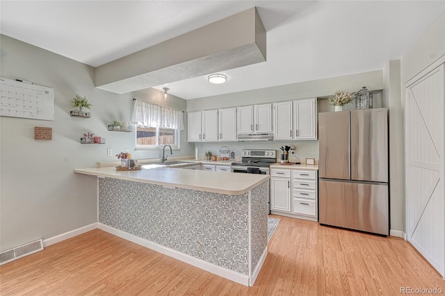 kitchen featuring light countertops, a peninsula, under cabinet range hood, stainless steel appliances, and visible vents