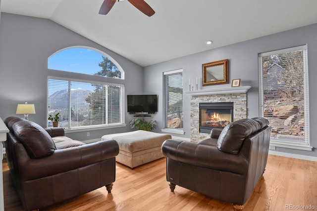 living area featuring a ceiling fan, lofted ceiling, a fireplace, and light wood finished floors