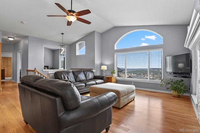 living room with ceiling fan with notable chandelier, baseboards, light wood-style floors, and vaulted ceiling