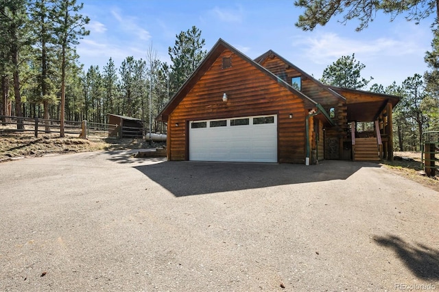 view of side of home with gravel driveway, a garage, fence, an outdoor structure, and log siding