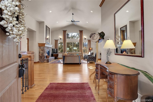 living room featuring ceiling fan, a fireplace, vaulted ceiling, and light wood-type flooring