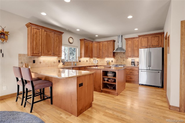 kitchen featuring wall chimney range hood, light hardwood / wood-style flooring, high quality fridge, a kitchen bar, and kitchen peninsula