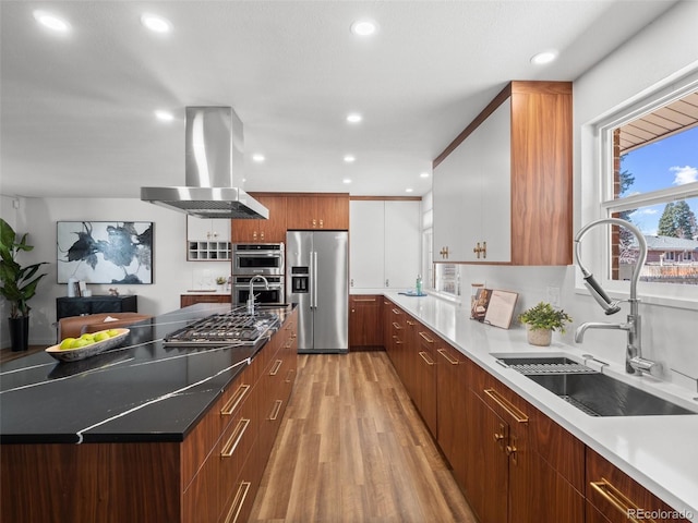 kitchen featuring island range hood, modern cabinets, appliances with stainless steel finishes, light wood-style floors, and a sink