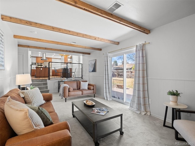 living room featuring light carpet, visible vents, beam ceiling, and wainscoting