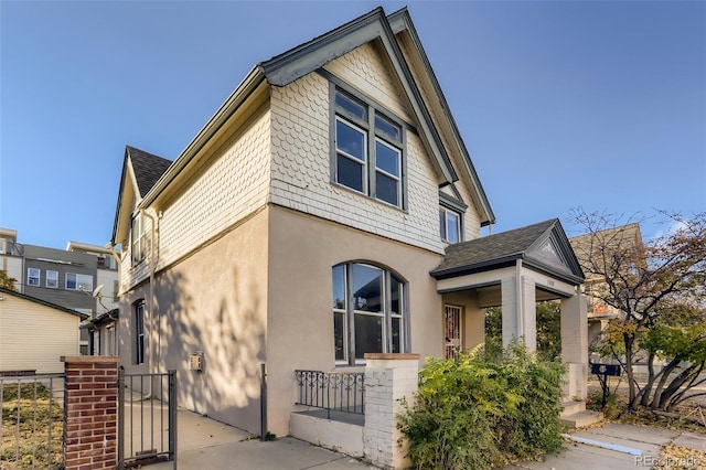 view of side of home with a shingled roof, fence, a gate, and stucco siding