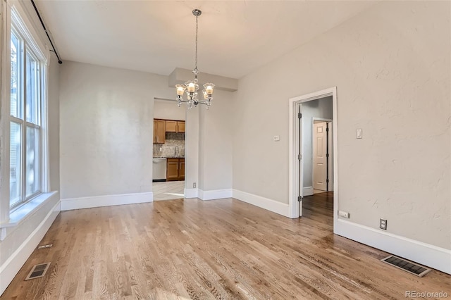 unfurnished dining area with plenty of natural light, a chandelier, and light hardwood / wood-style floors