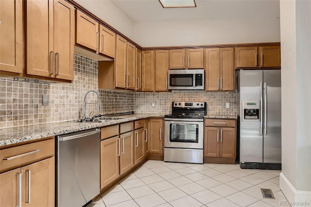 kitchen featuring sink, light tile patterned floors, stainless steel appliances, light stone countertops, and decorative backsplash