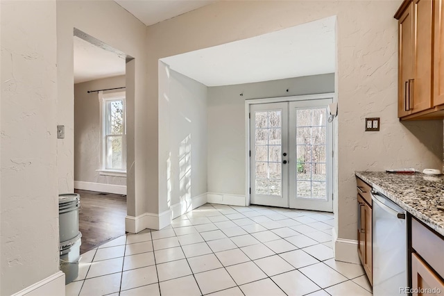 interior space with light stone counters, stainless steel dishwasher, french doors, and light tile patterned flooring