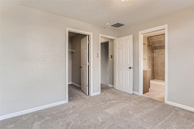 unfurnished bedroom with ensuite bath, a spacious closet, a textured ceiling, a closet, and light colored carpet