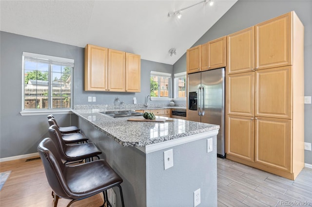19937 E Loyola Pl, Aurora, CO 80013 - kitchen featuring stainless steel appliances, light brown cabinetry, a kitchen bar, light wood-type flooring, and vaulted ceiling