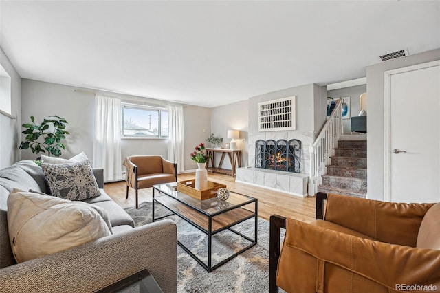 living room featuring stairs, visible vents, wood finished floors, and a tile fireplace