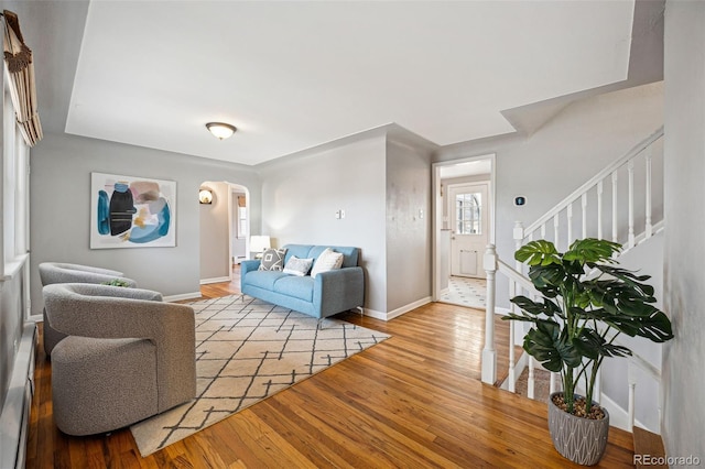 living area featuring arched walkways, light wood-style flooring, baseboards, stairs, and baseboard heating