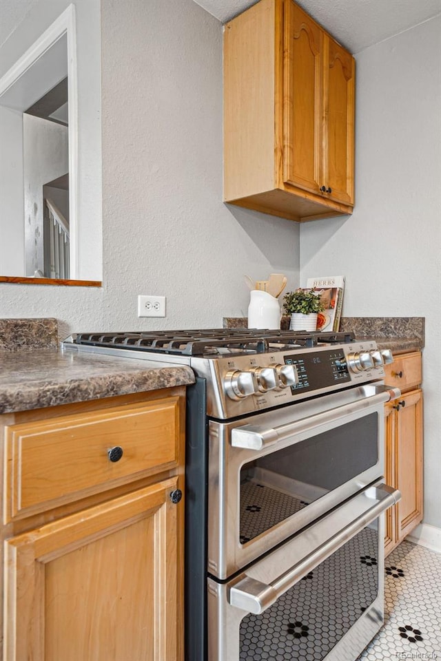 kitchen with stainless steel gas stove, light tile patterned floors, and dark stone counters