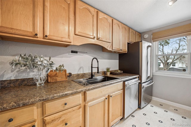 kitchen featuring appliances with stainless steel finishes, dark countertops, a sink, and baseboards